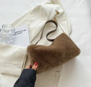 Brown faux fur shoulder bag on cream blazer, hand holding, glass decor and book nearby