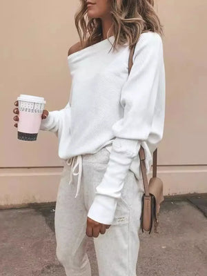 Woman wearing off-shoulder white sweater and light gray joggers, holding coffee cup