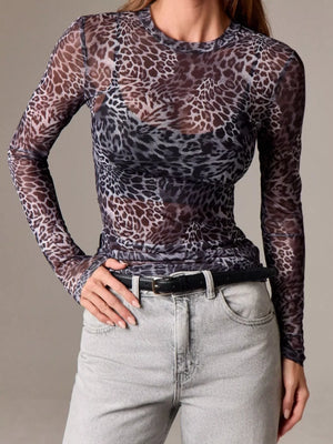 Woman wearing a sheer long-sleeve leopard print top with light-wash jeans and black belt