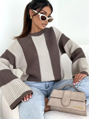 Woman wearing oversized striped knit sweater, light jeans, white cat-eye sunglasses, and holding beige Jacquemus handbag