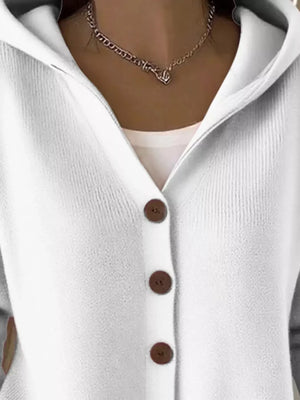 White knit cardigan with brown buttons, hood, and a chain necklace, close-up view