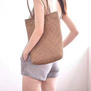 Woman wearing gray shorts and a woven straw tote bag, standing in bright light