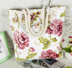 Floral canvas tote bag with rope handles, pink flower pattern, displayed on a white table