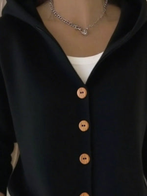 Black button-up cardigan with tan buttons, layered over a white top, worn with a chain necklace