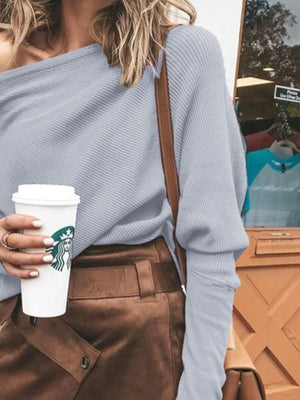 Woman in a light blue off-shoulder ribbed sweater and brown high-waisted skirt holding coffee