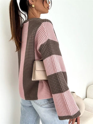 Woman wearing a pink and brown colorblock knit sweater, light jeans, and gold earrings