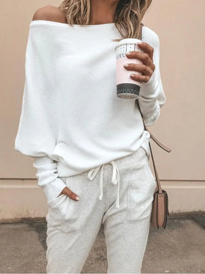 Woman in white off-shoulder sweater and light joggers holding coffee, casual fashion style
