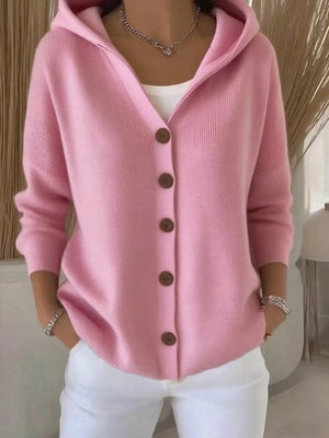 Woman wearing a pink button-up knit hoodie cardigan with white pants in a modern room.