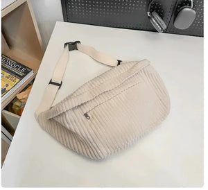 Beige corduroy crossbody bag with adjustable strap and zipper pocket on white desk