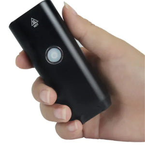 Hand holding a black portable electronic device with circular button and hot warning symbol