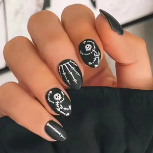 Hand with matte black Halloween nail art featuring skeleton and bone designs.
