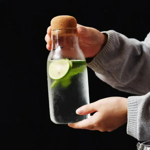Hand holding a glass carafe with cork lid, filled with water, lime slices, and mint