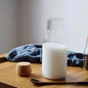 Glass milk bottle with cork lid on wooden tray, blue cloth and wooden spoon nearby