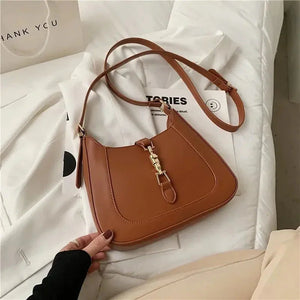 Brown leather shoulder bag with gold buckle detail on a bed, crossbody purse fashion accessory