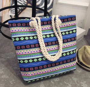 Colorful boho striped tote bag with rope handles, placed on a stone floor