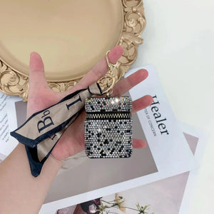 Hand holding a rhinestone-studded AirPods case with keychain and a beige ribbon