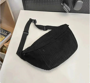 Textured black crossbody sling bag with adjustable strap on a white table