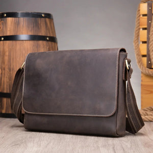 Brown leather messenger bag with shoulder strap on wooden surface, rustic background