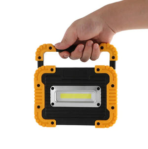Hand holding portable yellow and black LED work light with rugged handle