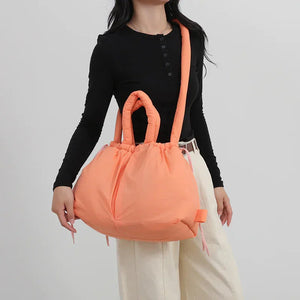 Woman wearing a black top and cream pants holding a large orange puffer tote bag