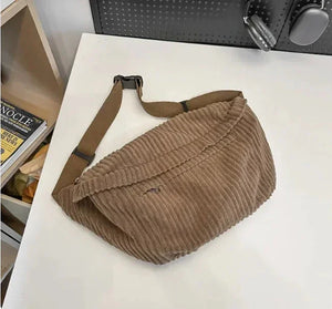 Textured brown corduroy crossbody bag with adjustable strap on white table