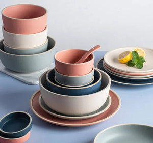 Stacked ceramic dinnerware set in pastel pink, blue, and cream, including plates and bowls.