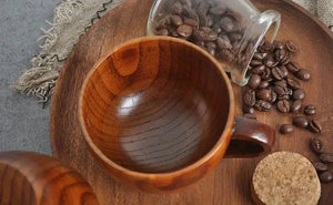 Wooden coffee cup on a wooden tray with scattered coffee beans and glass jar