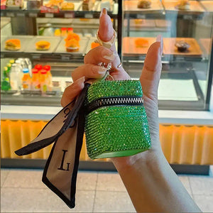 Hand holding a green rhinestone keychain pouch with zipper and attached scarf, bakery background