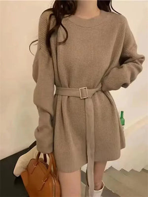 Woman in long-sleeve beige knit sweater dress with belt, holding a brown handbag