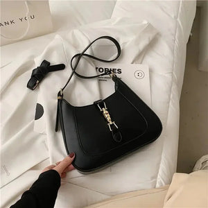 Black leather shoulder bag with gold hardware on white bedding