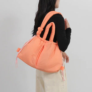 Woman carrying oversized peach puffer tote bag with knotted handles, casual outfit