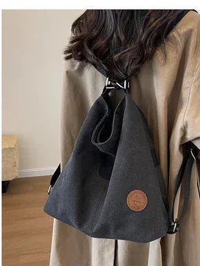 Woman wearing a black canvas backpack with leather patch, casual indoor setting