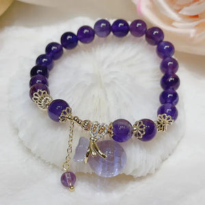 Purple beaded gemstone bracelet with gold accents and decorative charms on a soft surface