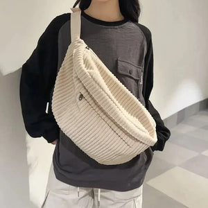 Woman wearing a large cream corduroy crossbody bag with ribbed texture and casual outfit