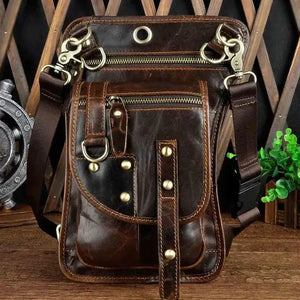 Brown leather crossbody bag with multiple zippers, rivets, and adjustable strap on a wooden surface