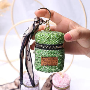 Hand holding small green rhinestone-studded mini bag keychain with zipper and ribbon