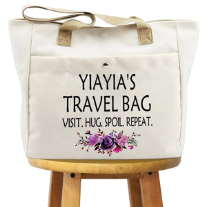 Beige canvas tote bag with text 'YiaYia's Travel Bag' and purple floral design on a stool