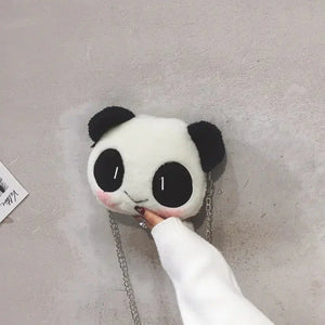 Cute fluffy panda face shoulder bag with chain strap held against a textured wall