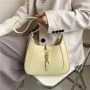Woman holding a pale yellow leather shoulder bag with buckle detail, neutral outfit