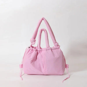 Soft pink puffer handbag with knotted handles and drawstring details on a white background
