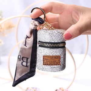 Hand holding a sparkly rhinestone keychain purse with zipper and decorative scarf accent