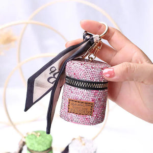 Hand holding small pink rhinestone keychain purse with zipper and attached scarf