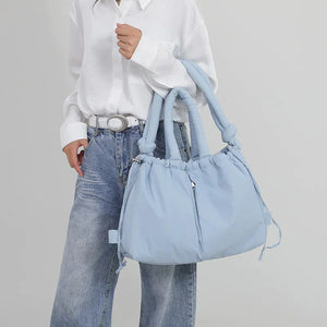 Woman wearing blue jeans and white shirt holding a large light blue shoulder bag