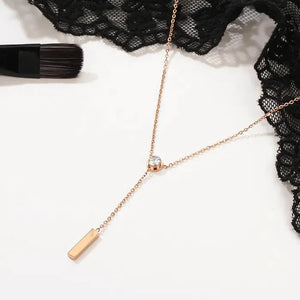 Gold Y-shaped necklace with clear gemstone and bar pendant on lace background