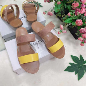 Women's open-toe sandals with yellow and tan suede straps on display boxes beside pink flowers