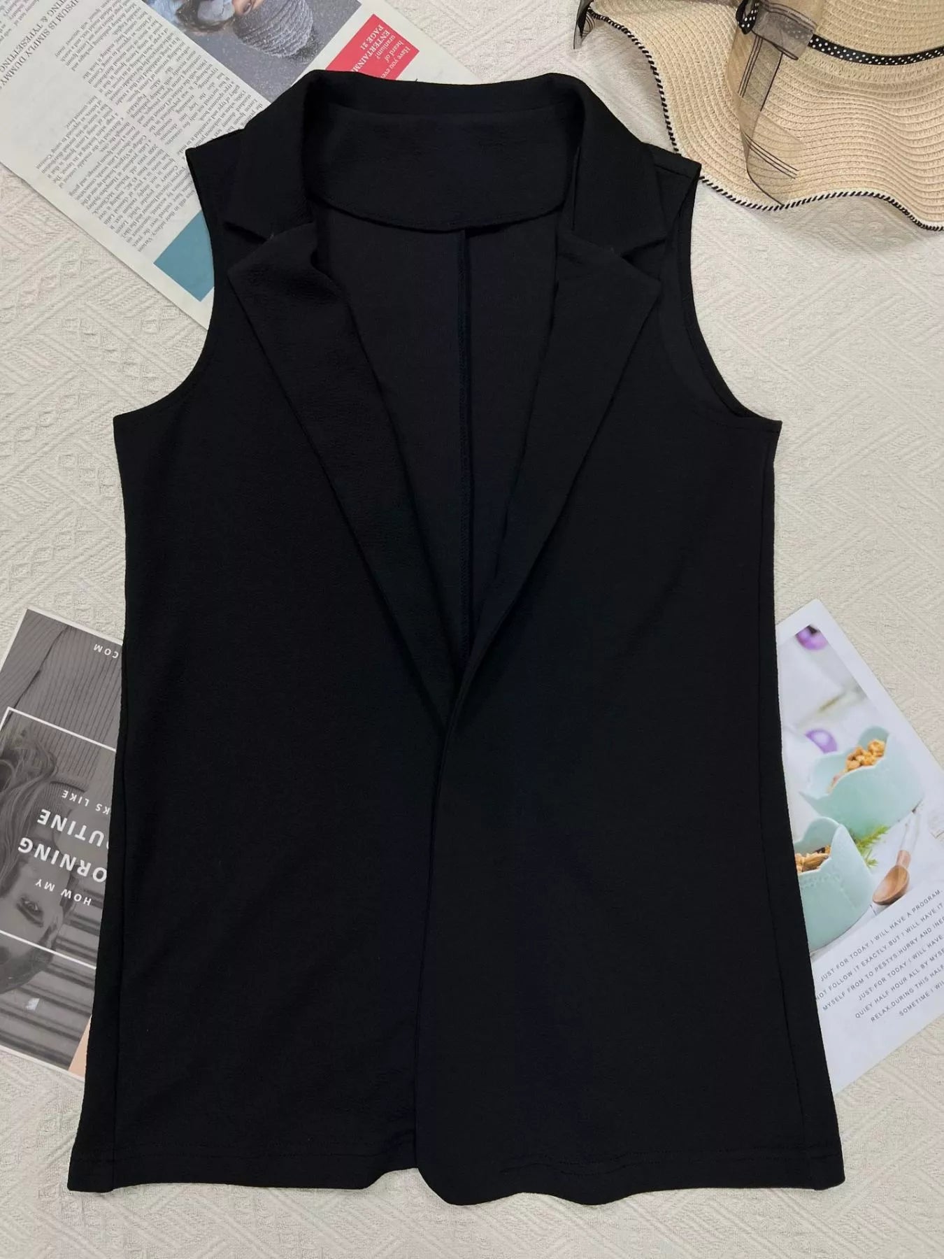 Black sleeveless blazer vest for women, stylish office wear with notched lapel, laid on magazine background