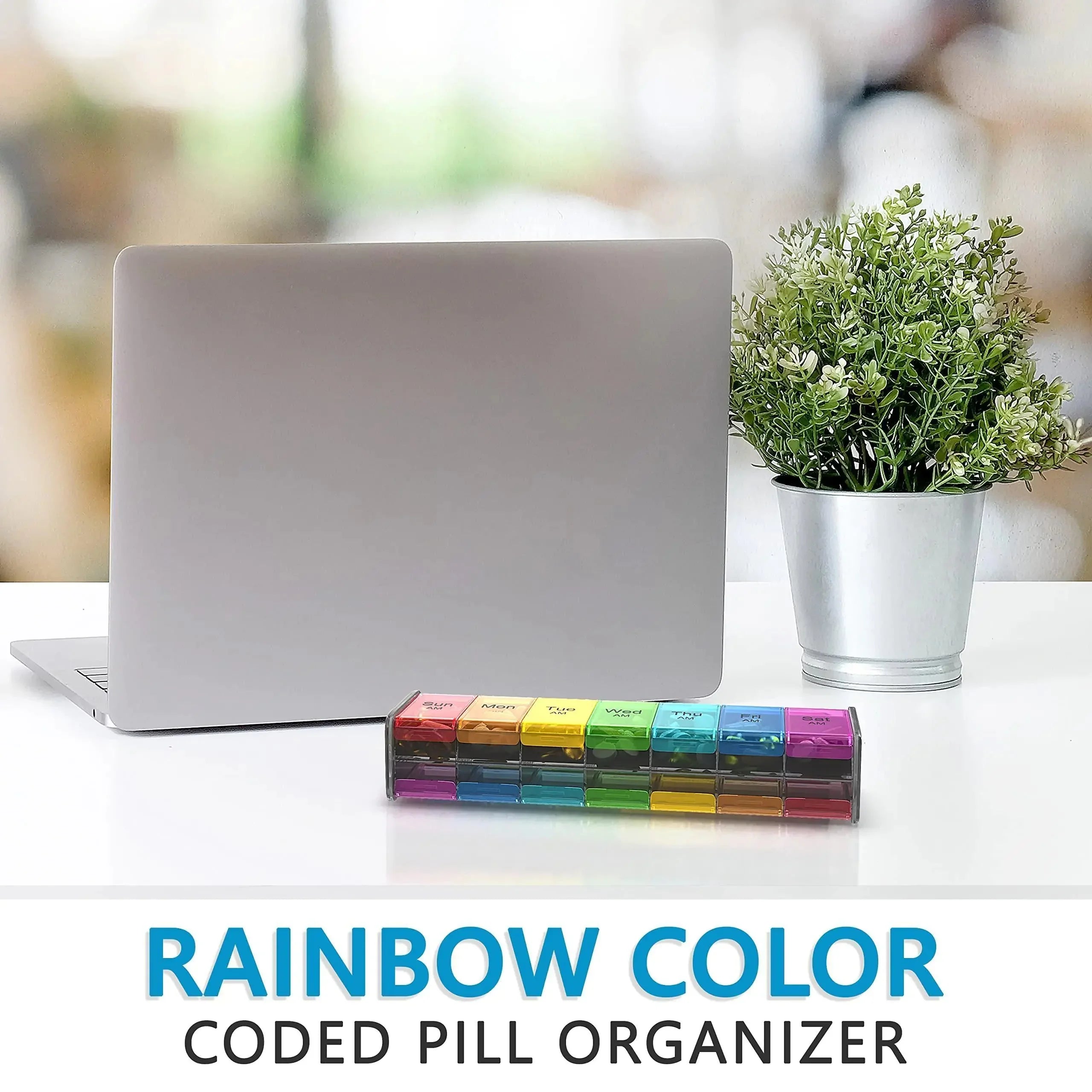 Rainbow color pill organizer on desk with laptop and potted plant, medication storage