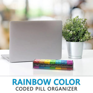 Rainbow color pill organizer on desk with laptop and potted plant, medication storage